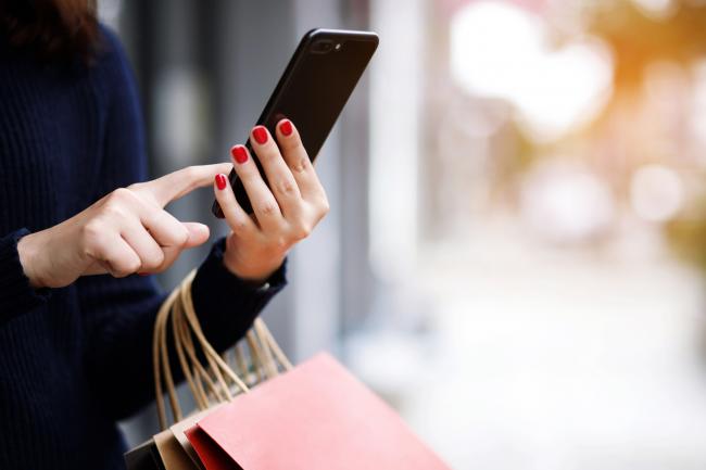 A woman on her phone holding shopping bags. Credit: Canva